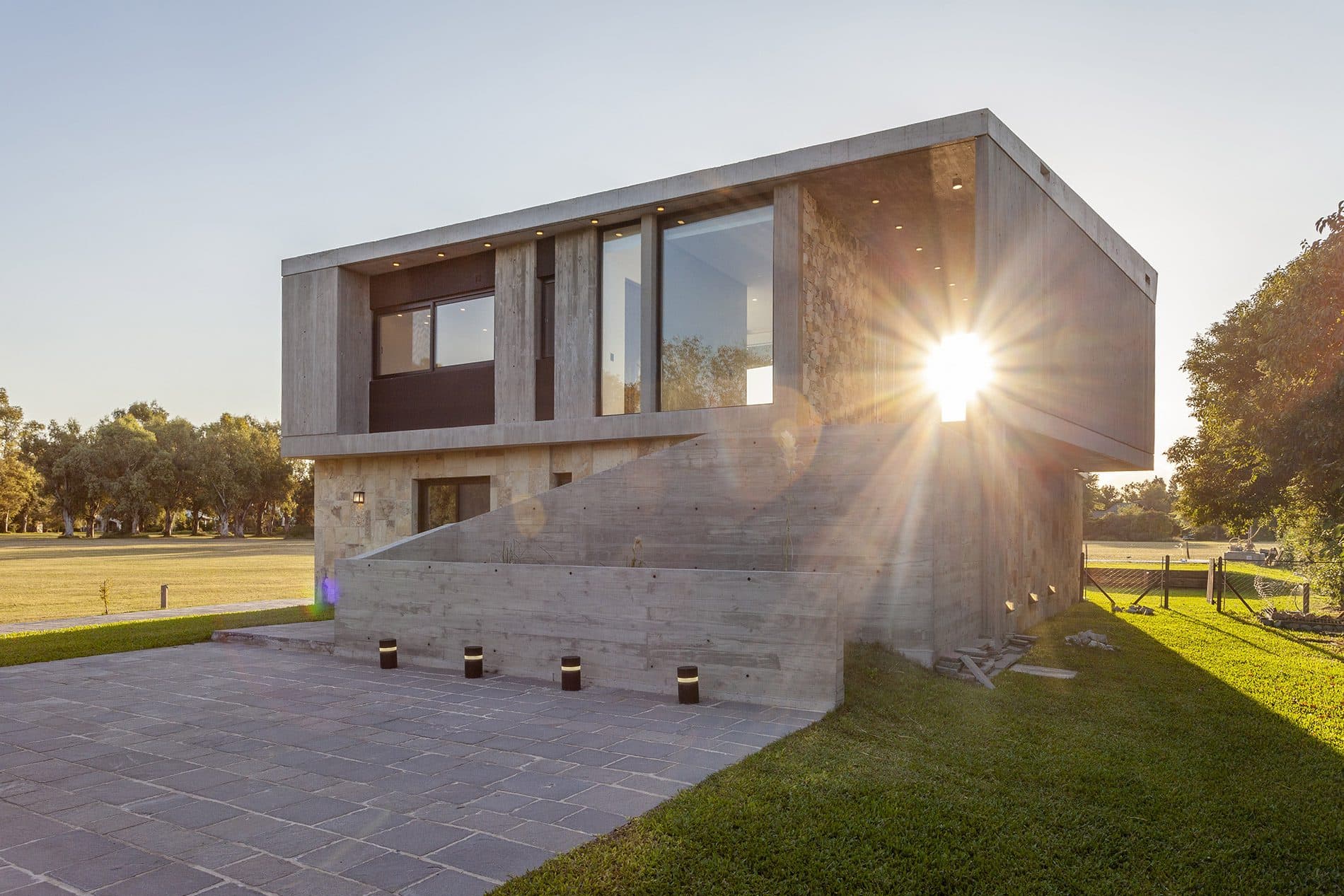 Stone and concrete house at sunset, with the sun between its volumes