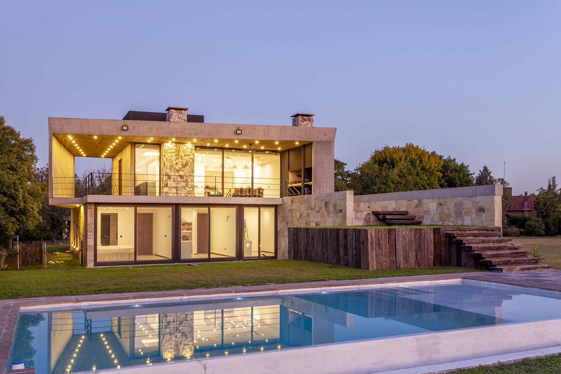 Stone and concrete house lit at dusk, with the pool in the foreground